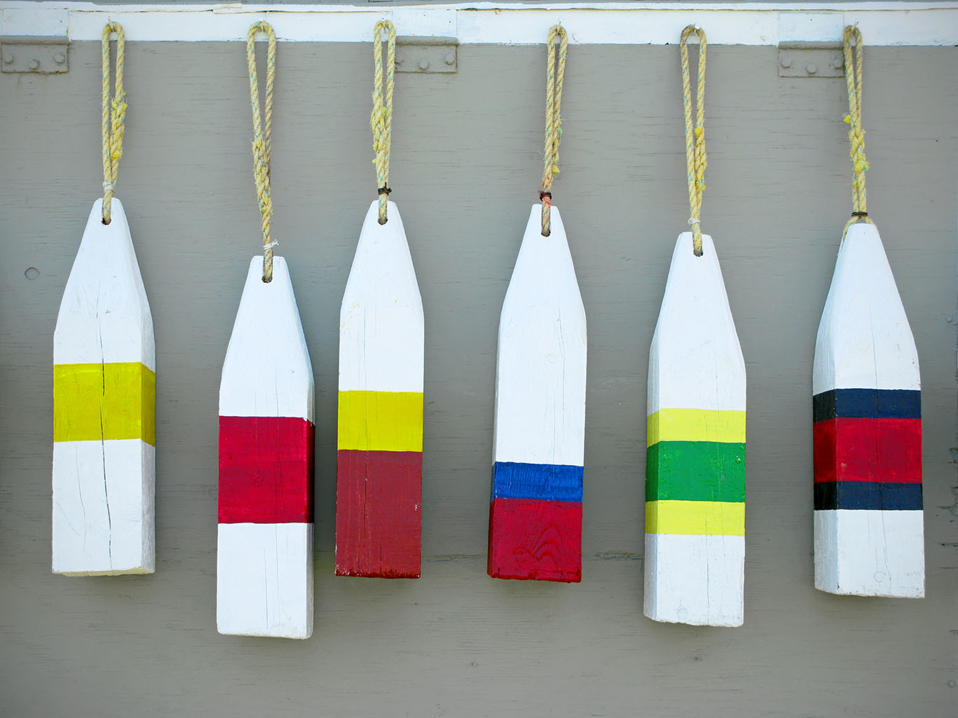 Wooden Lobster fishing buoys traditional to Atlantic Canada and the New England states. The buoys were painted in colours  that were unique to each boat. These ones are hanging in front of grey plywood.